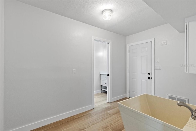 clothes washing area with baseboards, a textured ceiling, light wood-style floors, visible vents, and a sink