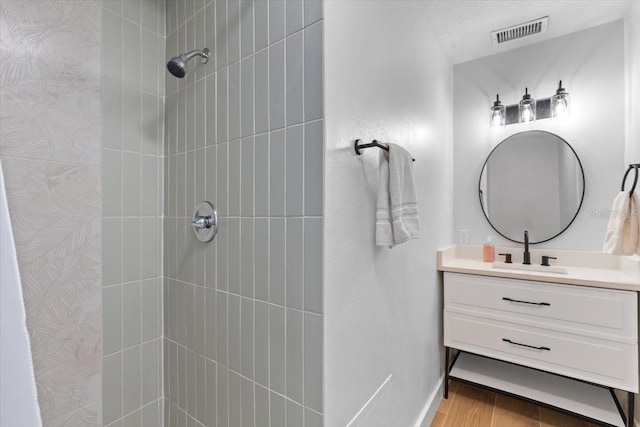 full bathroom with tiled shower, vanity, visible vents, and wood finished floors