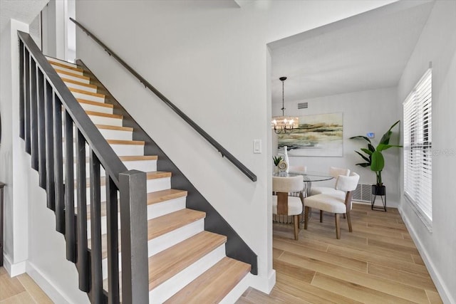 stairway featuring wood finished floors, baseboards, visible vents, and a notable chandelier