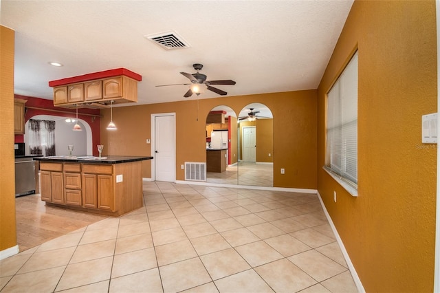 kitchen with arched walkways, dark countertops, a ceiling fan, and visible vents