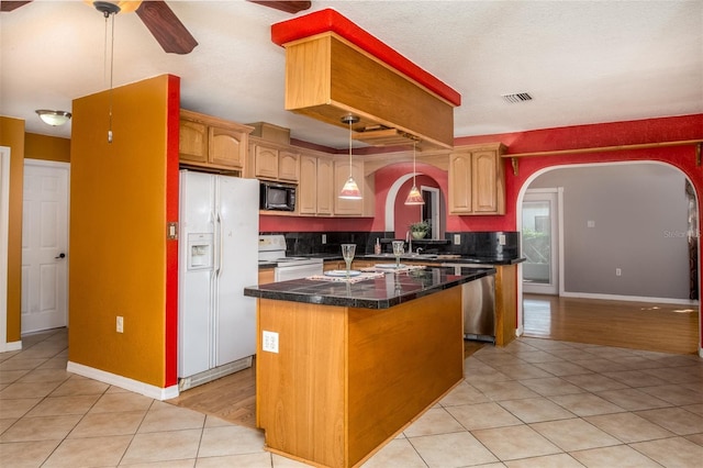 kitchen with arched walkways, light tile patterned floors, white appliances, and a center island