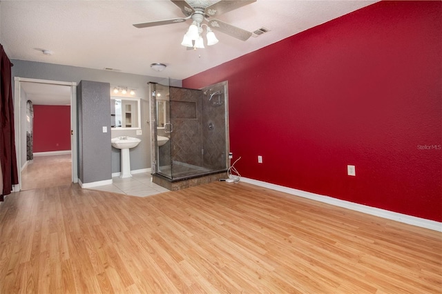 interior space with visible vents, baseboards, a ceiling fan, light wood finished floors, and ensuite bath