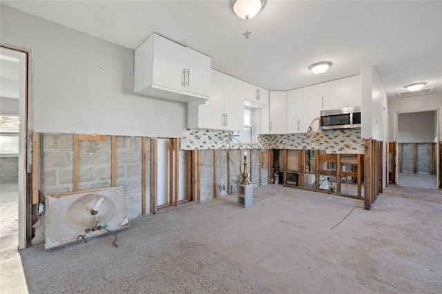 kitchen featuring stainless steel microwave, unfinished concrete flooring, and white cabinetry