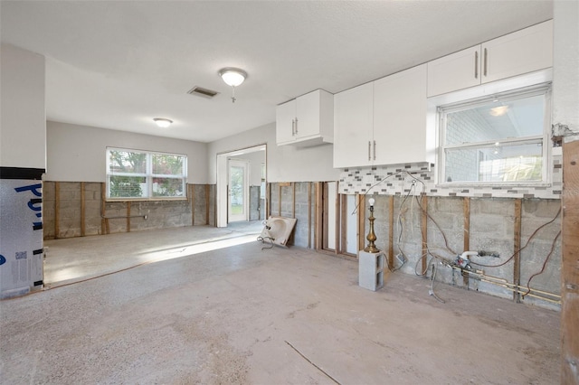 kitchen with white cabinets, visible vents, and concrete flooring