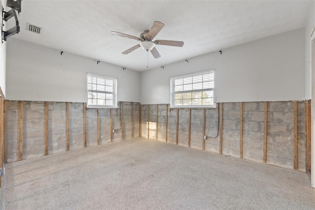 carpeted spare room with a ceiling fan, visible vents, and a healthy amount of sunlight