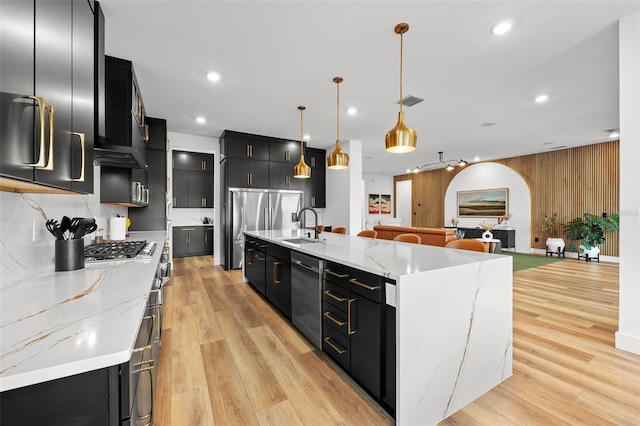 8720 Drummer Plank Dr, Wesley Chapel, FL 33545 - kitchen featuring hanging light fixtures, appliances with stainless steel finishes, light wood finished floors, dark cabinetry, and a spacious island