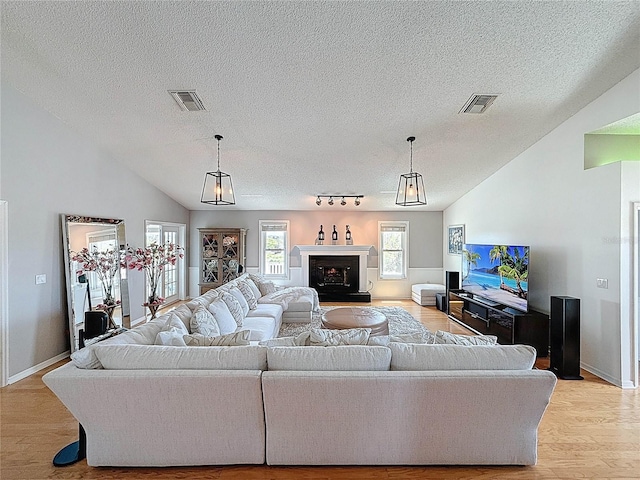 living room with a textured ceiling, light wood-type flooring, vaulted ceiling, and baseboards