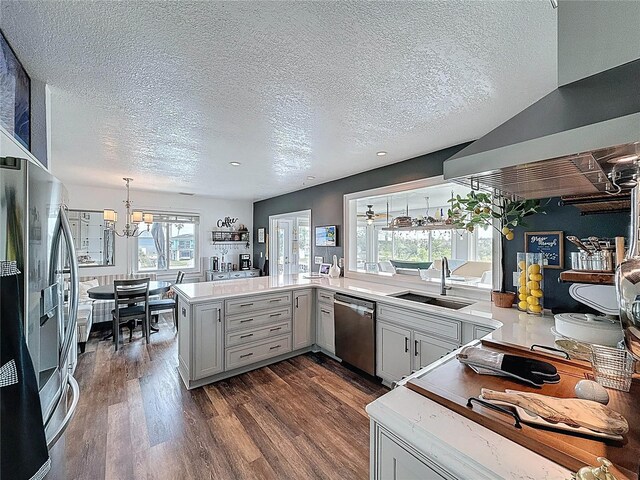 kitchen with stainless steel appliances, a sink, a chandelier, a textured ceiling, and range hood