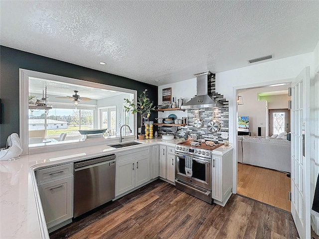 kitchen featuring stainless steel appliances, a sink, wall chimney exhaust hood, a textured ceiling, and light countertops