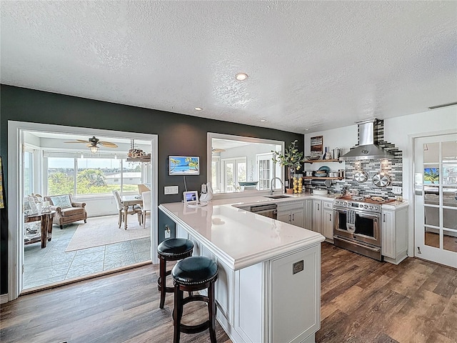 kitchen featuring stainless steel stove, wall chimney range hood, a textured ceiling, light countertops, and dark wood finished floors