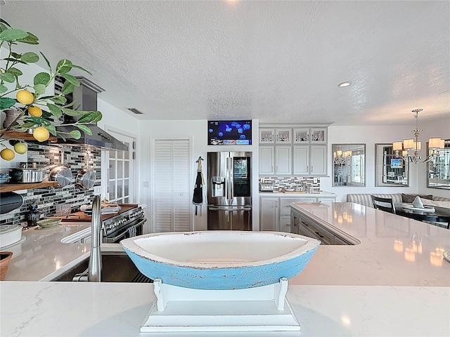 kitchen featuring stainless steel fridge, a chandelier, a textured ceiling, decorative backsplash, and glass insert cabinets
