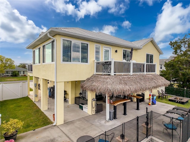 back of house featuring a patio, a gate, stucco siding, metal roof, and a balcony