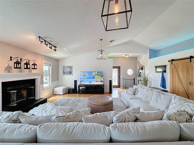 living room with a barn door, light wood-type flooring, lofted ceiling, a textured ceiling, and plenty of natural light