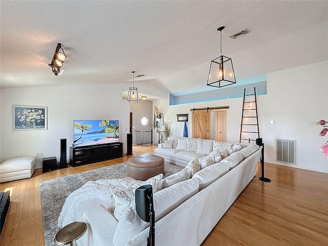 living area with a barn door, wood finished floors, lofted ceiling, a textured ceiling, and baseboards
