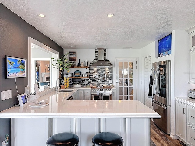 kitchen with wall chimney exhaust hood, stainless steel appliances, a sink, light countertops, and a peninsula
