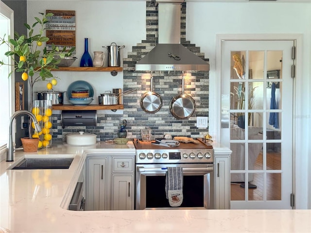 kitchen with stainless steel electric stove, a sink, wall chimney range hood, backsplash, and light countertops