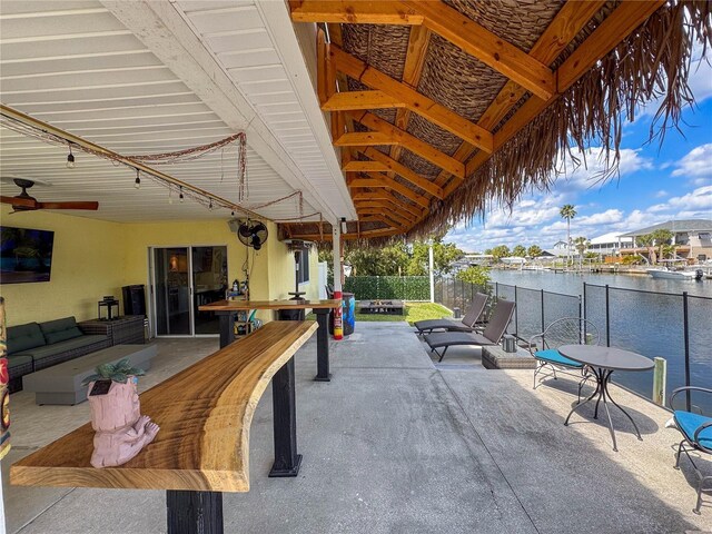 view of patio / terrace featuring a water view, an outdoor living space with a fire pit, fence, and a ceiling fan