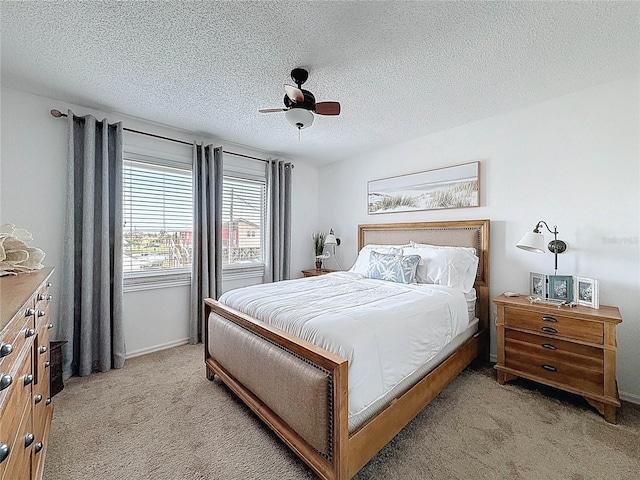 bedroom with light carpet, a textured ceiling, a ceiling fan, and baseboards