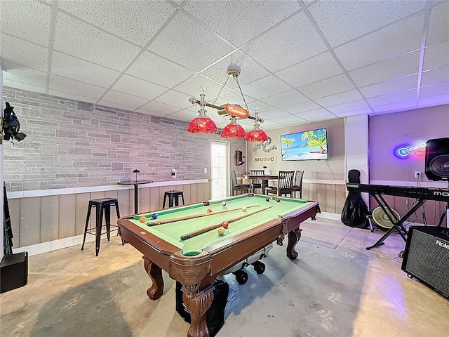 rec room with a paneled ceiling, unfinished concrete floors, pool table, and brick wall
