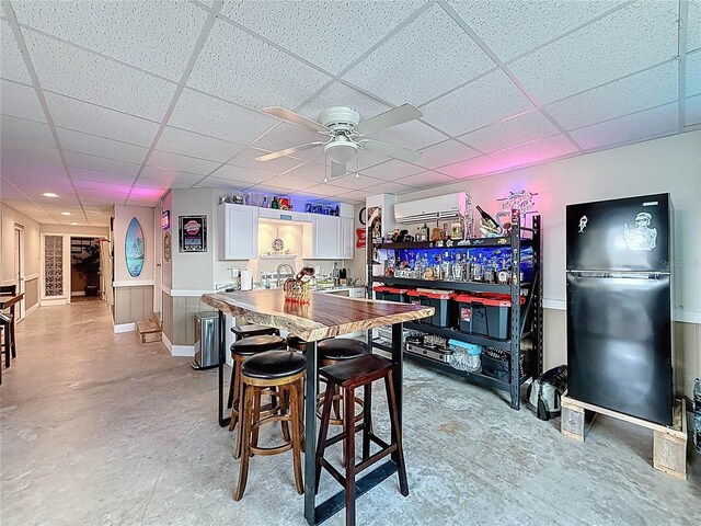 dining area with a ceiling fan, a wall mounted AC, a paneled ceiling, bar, and concrete flooring