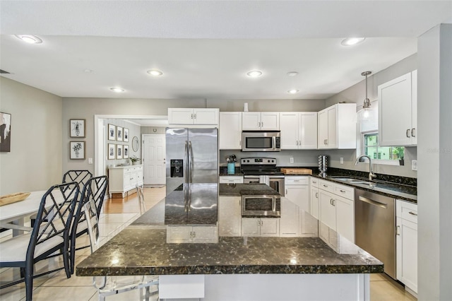 kitchen featuring a sink, a kitchen island, dark stone countertops, stainless steel appliances, and white cabinets