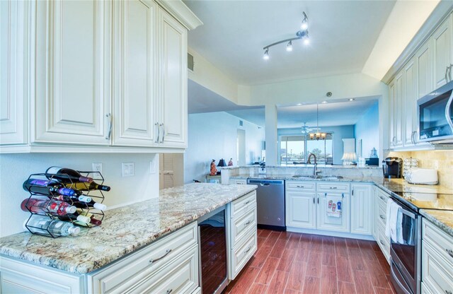 kitchen featuring a sink, beverage cooler, a peninsula, appliances with stainless steel finishes, and light stone countertops