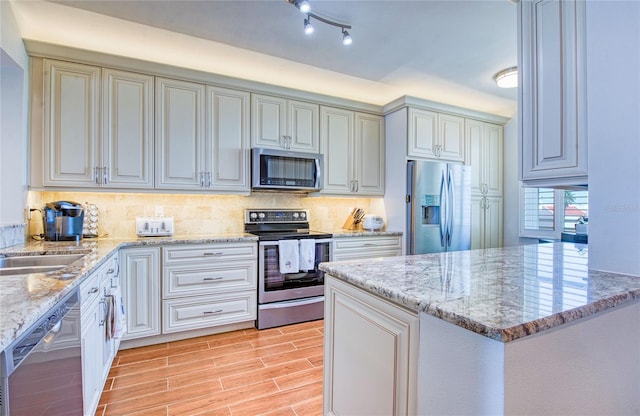 kitchen featuring light wood-style floors, light stone countertops, decorative backsplash, and stainless steel appliances