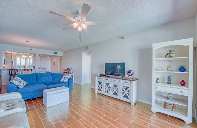 living area featuring ceiling fan with notable chandelier, baseboards, visible vents, and a textured ceiling