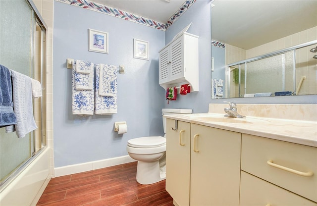 full bath featuring wood finished floors, toilet, vanity, baseboards, and bath / shower combo with glass door
