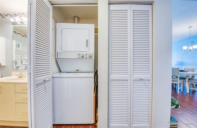 laundry area featuring laundry area, wood finished floors, a sink, stacked washing maching and dryer, and a chandelier
