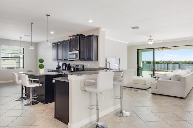 10008 Celtic Ash Dr, Ruskin, FL 33573 - kitchen featuring appliances with stainless steel finishes, a kitchen breakfast bar, light tile patterned flooring, crown molding, and open floor plan