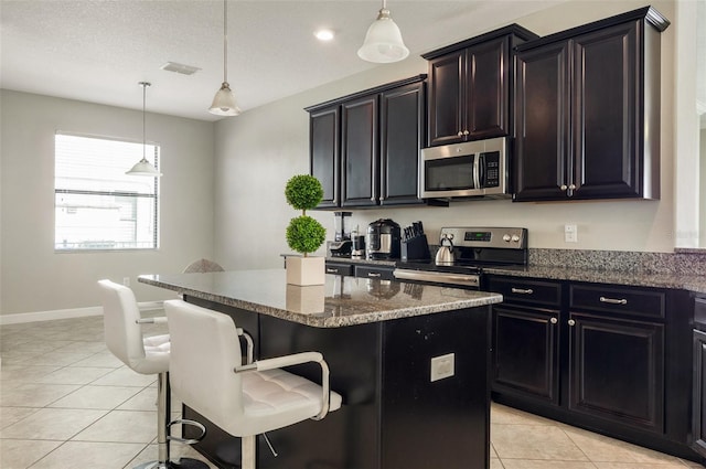 10008 Celtic Ash Dr, Ruskin, FL 33573 - kitchen featuring stainless steel appliances, light tile patterned flooring, a center island, a kitchen breakfast bar, and dark stone counters