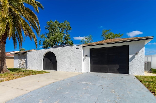 ranch-style home with an outdoor structure, stucco siding, central air condition unit, driveway, and a garage