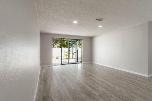 unfurnished room featuring baseboards, visible vents, a textured ceiling, and wood finished floors