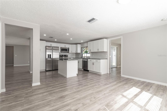 kitchen with dark countertops, appliances with stainless steel finishes, light wood-style floors, open floor plan, and backsplash