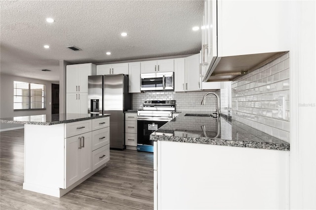 kitchen featuring decorative backsplash, visible vents, appliances with stainless steel finishes, white cabinetry, and a sink