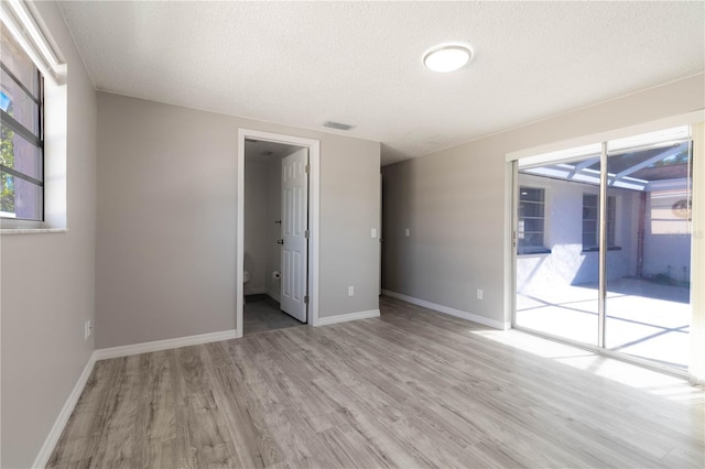 spare room featuring baseboards, visible vents, a textured ceiling, and wood finished floors
