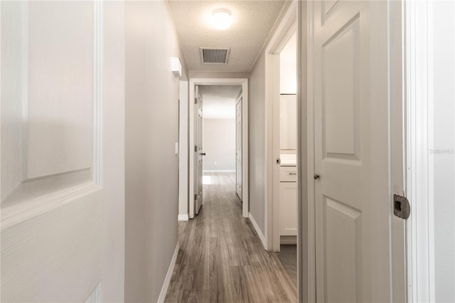 corridor featuring wood finished floors, visible vents, baseboards, and a textured ceiling