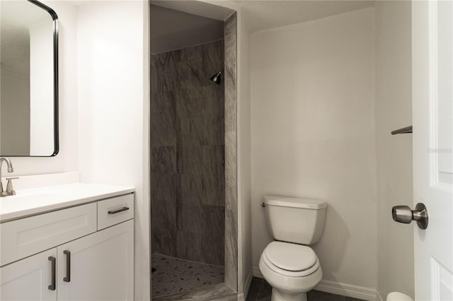bathroom with vanity, baseboards, toilet, and tiled shower