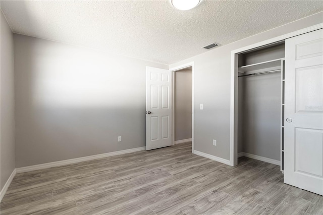 unfurnished bedroom featuring baseboards, a textured ceiling, light wood-style floors, visible vents, and a closet