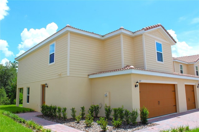 view of side of home with a tiled roof, stucco siding, and a garage