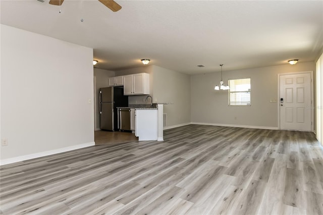 unfurnished living room with ceiling fan with notable chandelier, baseboards, light wood finished floors, and a sink