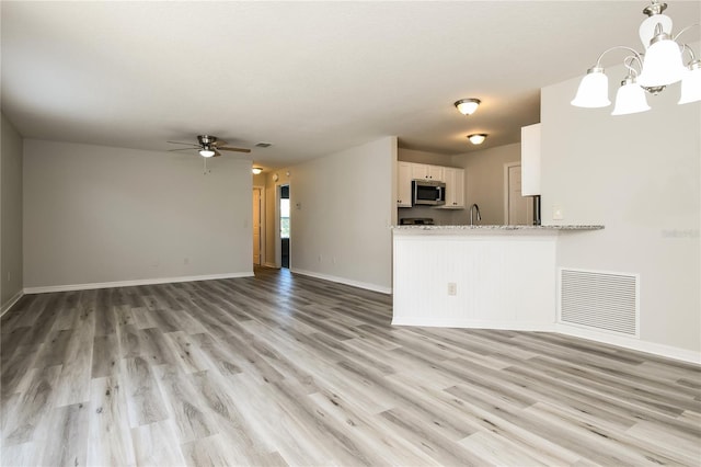 unfurnished living room featuring light wood-style flooring, visible vents, baseboards, and ceiling fan with notable chandelier