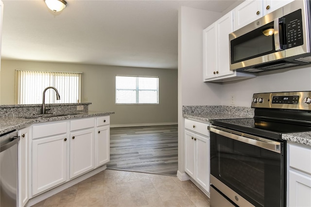 kitchen with light stone counters, a sink, stainless steel appliances, white cabinets, and baseboards