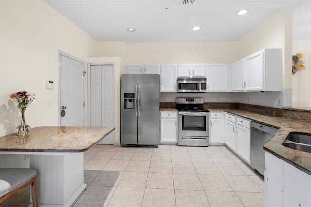 11260 Kapok Grand Cir, Madeira Beach, FL 33708 - kitchen with dark stone countertops, light tile patterned floors, white cabinetry, recessed lighting, and stainless steel appliances