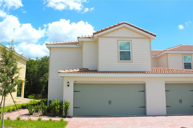 view of front facade with an attached garage, a tile roof, stucco siding, and driveway