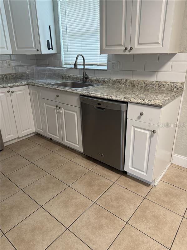 kitchen featuring white cabinetry, tasteful backsplash, stainless steel dishwasher, a sink, and light tile patterned flooring