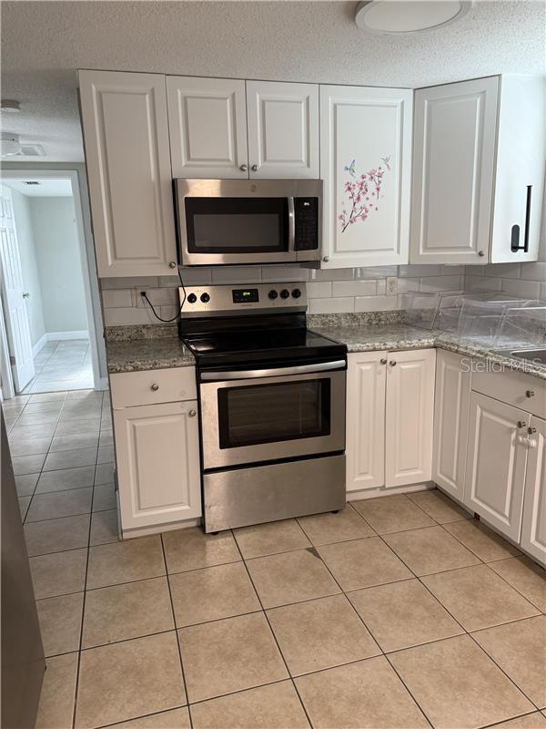 kitchen featuring white cabinets, decorative backsplash, light tile patterned floors, and stainless steel appliances