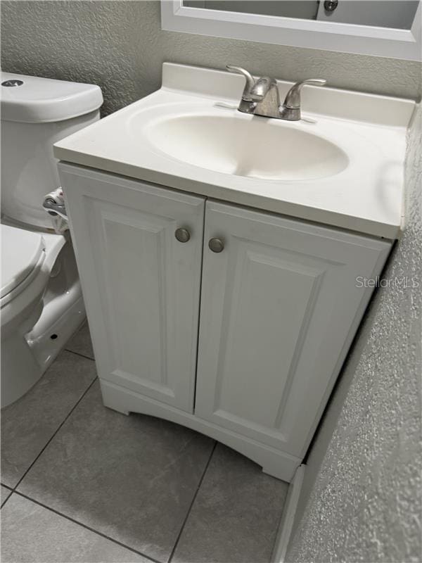 bathroom featuring toilet, a textured wall, tile patterned flooring, and vanity