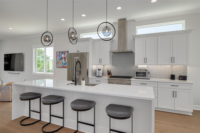 kitchen featuring a sink, stainless steel refrigerator, light wood-type flooring, wall chimney exhaust hood, and a kitchen bar